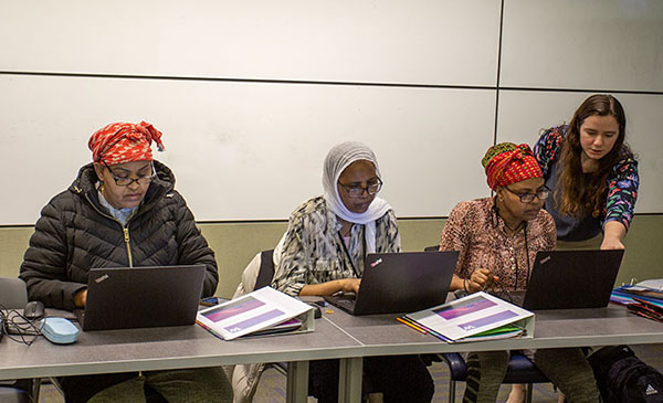 three people work on computers while a teacher leans over the shoulder of one student